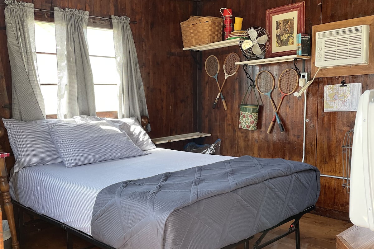 A wooden room with a bed, a shelf with books and a fan, and a map on the wall.