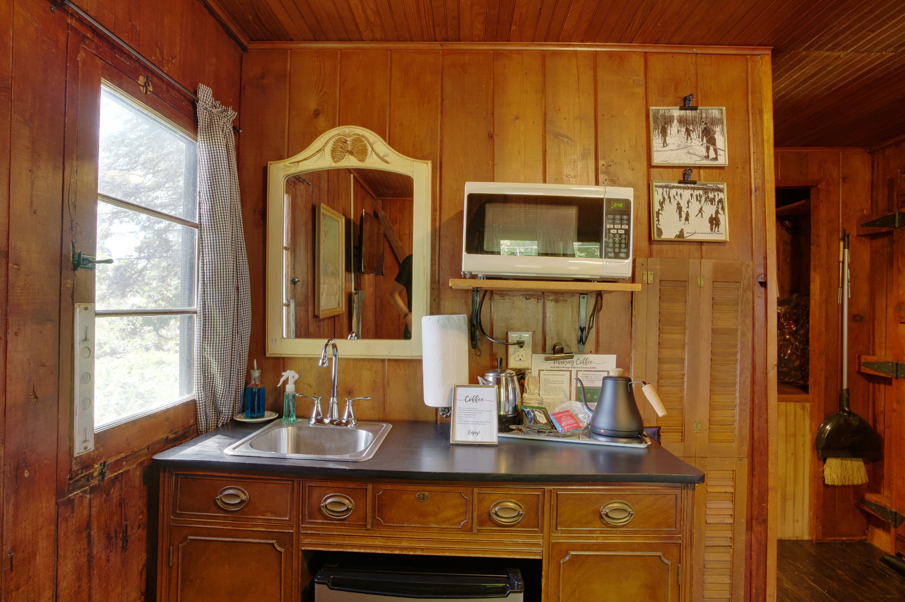Un baño de estilo cabaña de madera con lavamanos, espejo y un microondas encima.