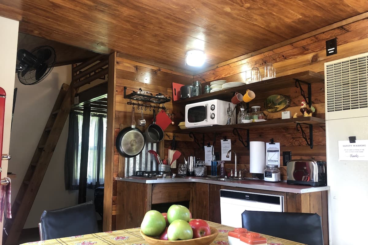 A kitchen with wooden walls, a microwave, a stove, and a sink. There is a table with a bowl of apples and a toy.