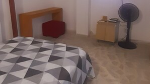 A bedroom with a bed, a TV, a fan, and a small cabinet.