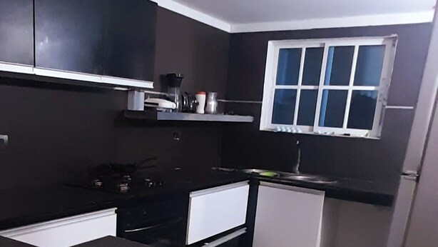 A compact kitchen with black countertops, white cabinets, and a window above the sink.