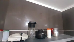 A kitchen counter with a coffee maker, a kettle, a thermos, a blender, and a small container.