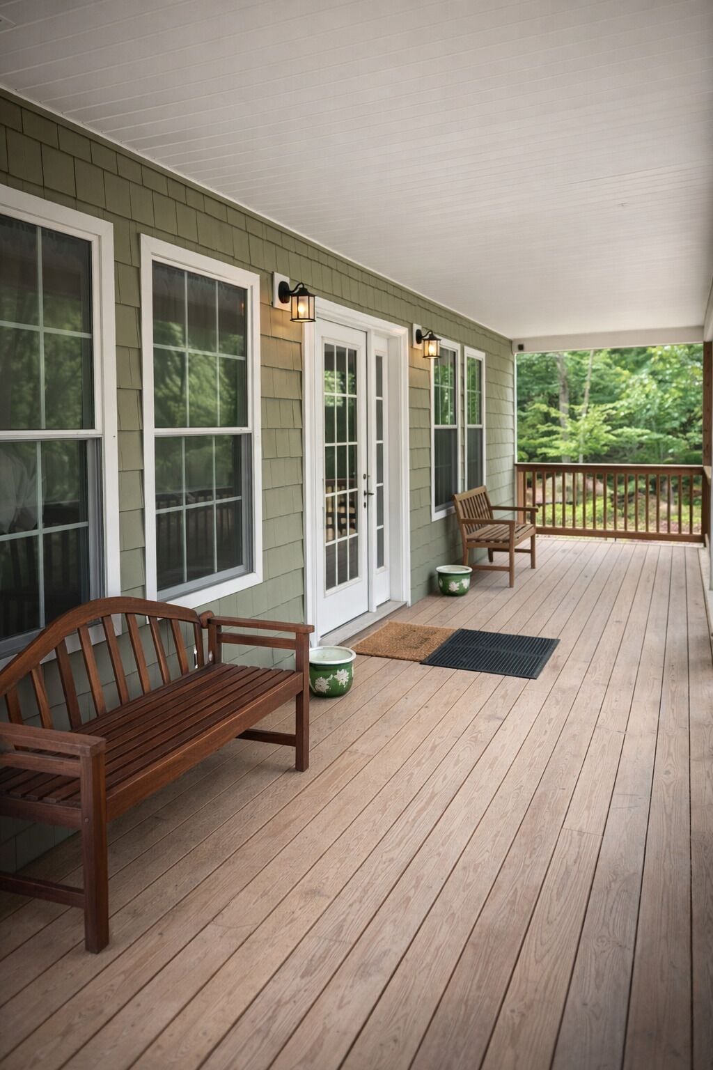 A covered porch with wooden flooring, two wooden benches, and a door with glass panels.