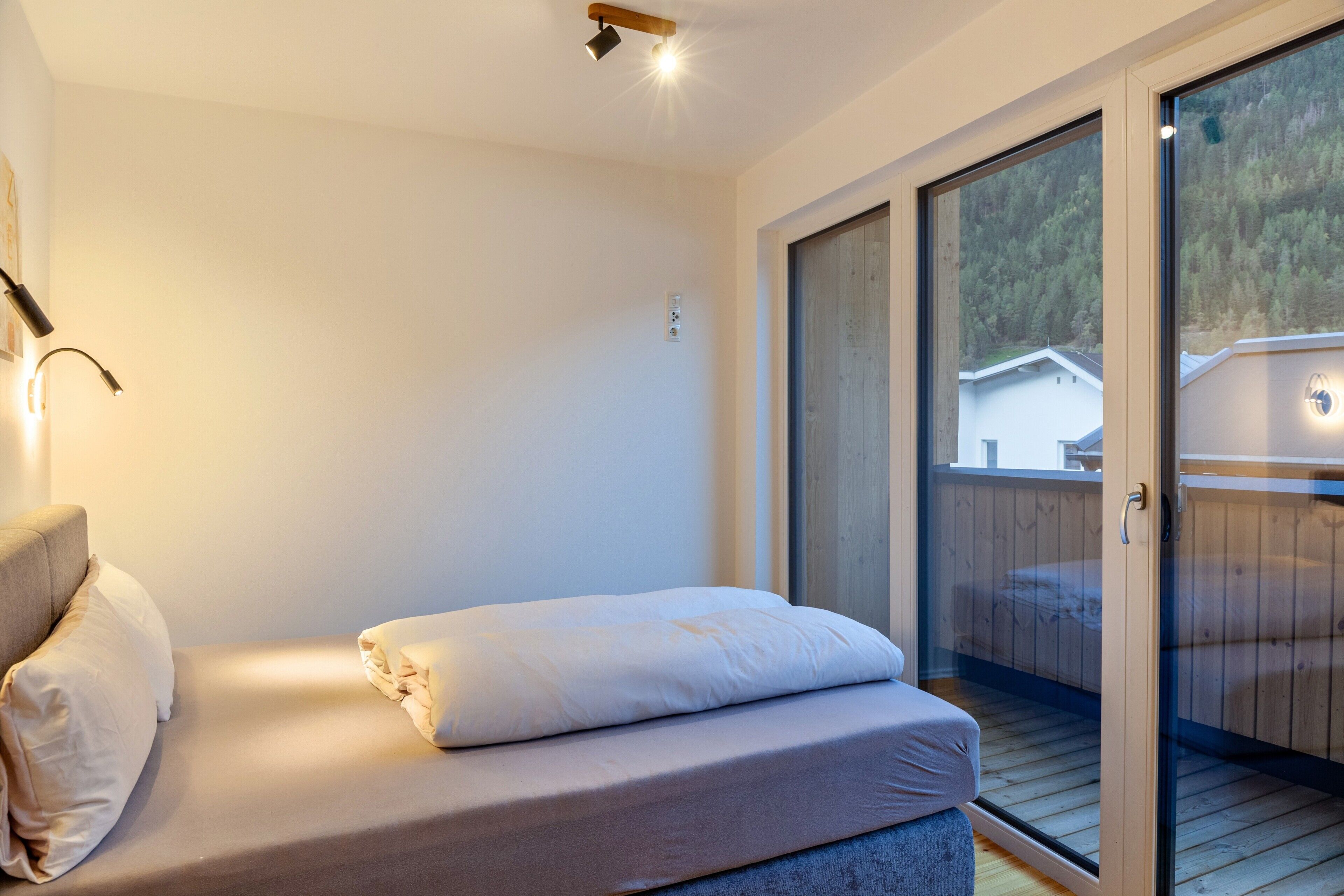 A bedroom with a bed, a nightstand, a lamp, and a sliding glass door leading to an outdoor deck.