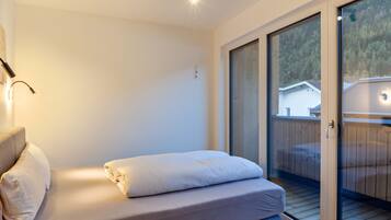 A bedroom with a bed, a nightstand, a lamp, and a sliding glass door leading to an outdoor deck.
