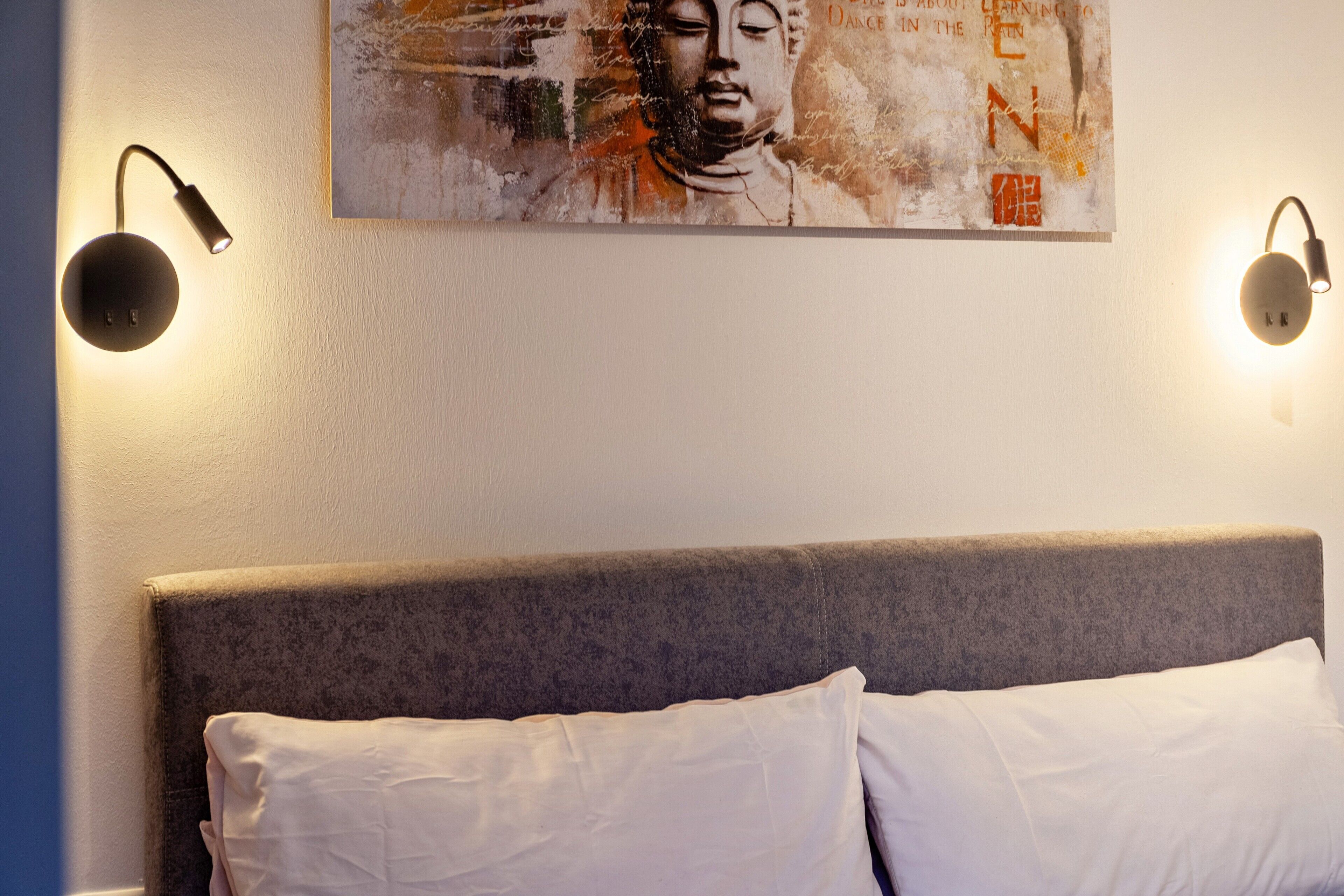 A bedroom with a bed, two wall-mounted lights, and a painting on the wall.