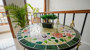 Una mesa redonda con una superficie de mosaico, una planta en maceta y una barandilla metálica.