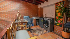 Una cocina compacta con pared de ladrillo, lavadora, una mesita con una silla y una planta en maceta.