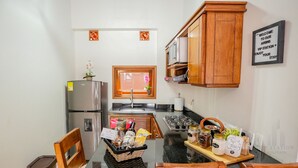 Una cocina compacta con armarios de madera, un refrigerador de acero inoxidable, un lavamanos y una zona de comedor con una mesa dispuesta para dos personas.