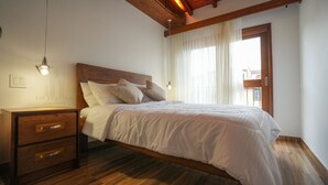 Una cama bien hecha con sábanas blancas, cabecera de madera y mesita de noche con cajones.