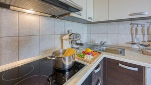 A modern kitchen with a stovetop, a pot of spaghetti, a cutting board with vegetables, and a sink.