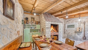 A rustic dining area with a stone fireplace, wooden beams, and a green cabinet.