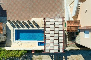 A swimming pool with a tiled deck, a stone wall, and a red-tiled roof.