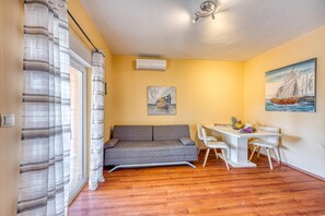 Ein Zimmer mit einer Couch, einem Esstisch mit Stühlen, einem Gemälde und einer Klimaanlage.