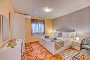 Habitación de hotel con cama, mesitas de noche, un escritorio, una silla, una ventana con cortinas y suelo con motivo de espiga.