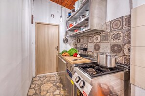 A compact kitchen with a gas stove, a cutting board with vegetables, and a hanging light fixture.