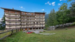 A multi-story hotel with balconies, a parking area, and a grassy landscape. - Appartamento 7 Bello Mountain View, Sauze d'Oulx, Italy (Sauze d'Oulx)