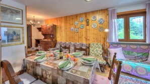 A dining area with a table set for four, a sofa, and a wooden wall with decorative plates. - Appartamento 7 Bello Mountain View, Sauze d'Oulx, Italy (Sauze d'Oulx)