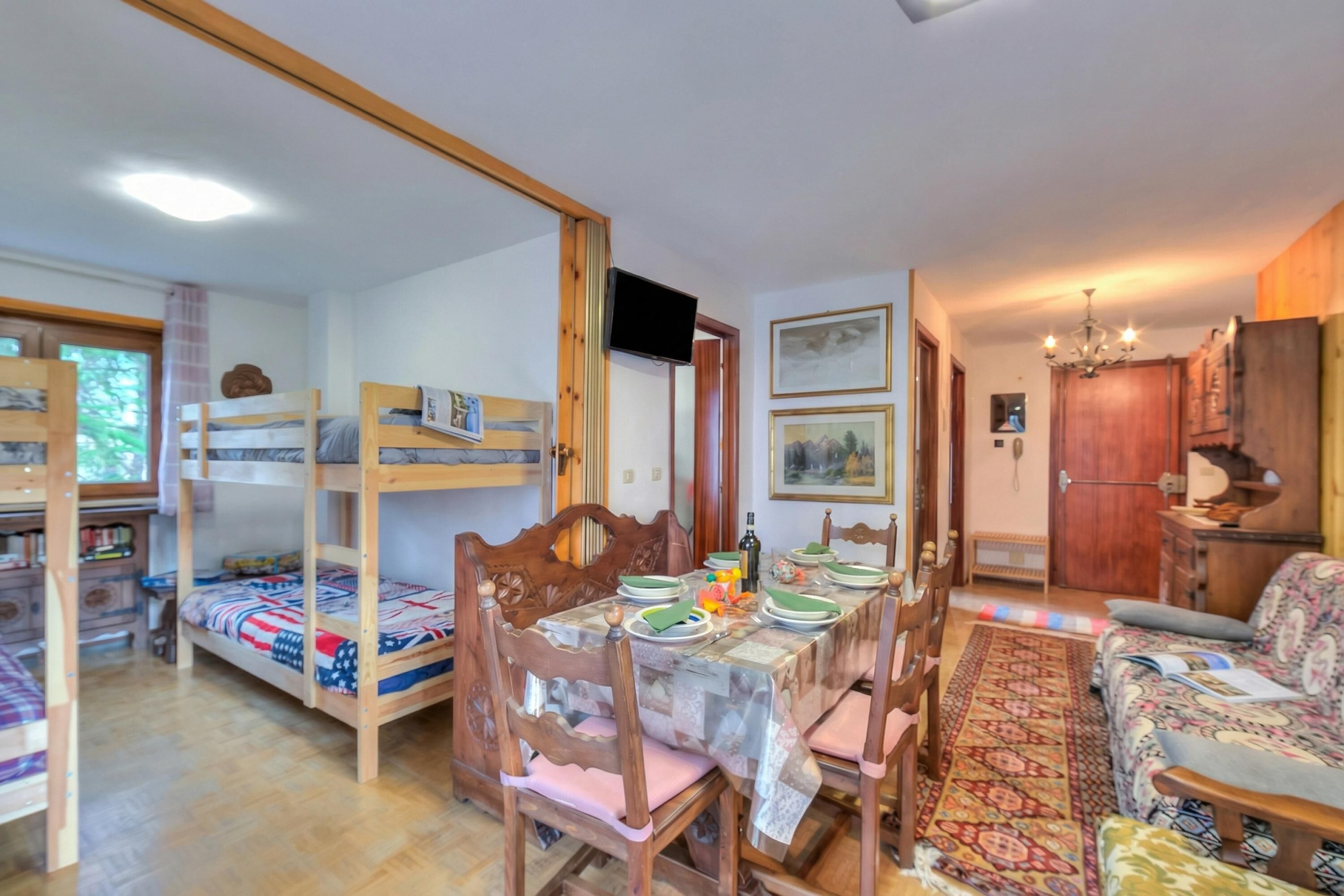 A room with bunk beds, a dining table with chairs, a sofa, and a television.