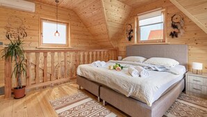 Een houten slaapkamer met een bed, nachtkastje, ramen en een dromenvanger.