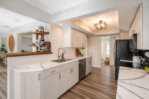 A modern kitchen with a central island, white cabinetry, and a black refrigerator. - Welcome to your dream oasis near the stunning Siesta Key! (Sarasota)