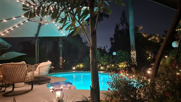 A pool area with a chair and umbrella, surrounded by plants and string lights. - Welcome to your dream oasis near the stunning Siesta Key!  (Sarasota)