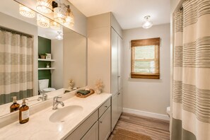Un baño moderno con un espejo grande, un lavabo y una ventana con persianas.