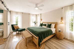 Un dormitorio con una cama, una silla, un banco, una mesita de noche y un ventanal.