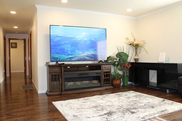 A living room with a large flat-screen TV, a wooden entertainment center, a fireplace, and a decorative plant. - Rare 1.5-acre gem—updated Home with Peaceful, private setting and serene. (Federal Way)