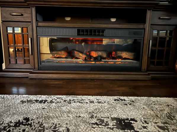 A fireplace with logs burning, wooden cabinets, and a patterned rug on the floor.