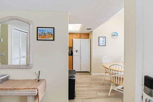 A compact kitchen with a refrigerator, a dining table with chairs, and a small trash bin.