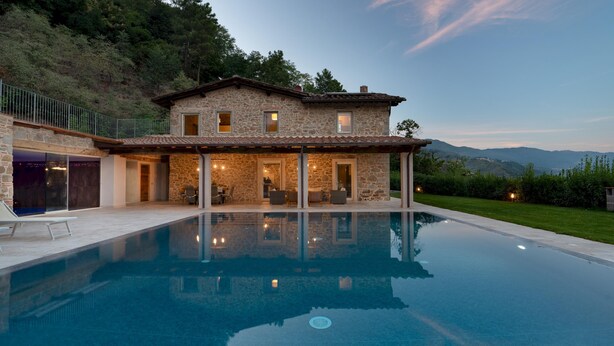 Una villa in pietra con piscina, area salotto esterna e vista sulle montagne.