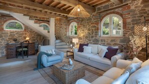 Un interno rustico in pietra con un divano bianco, una scrivania in legno e una scala.