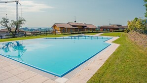 Una piscina rectangular con un borde de baldosas, rodeada de césped y una hilera de casas con tejados rojos.