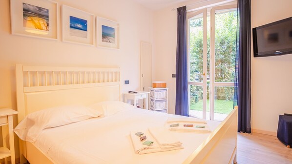 Ein Schlafzimmer mit einem Bett, einem Schreibtisch, einem Stuhl, einem Fernseher und einem Fenster mit Vorhängen.