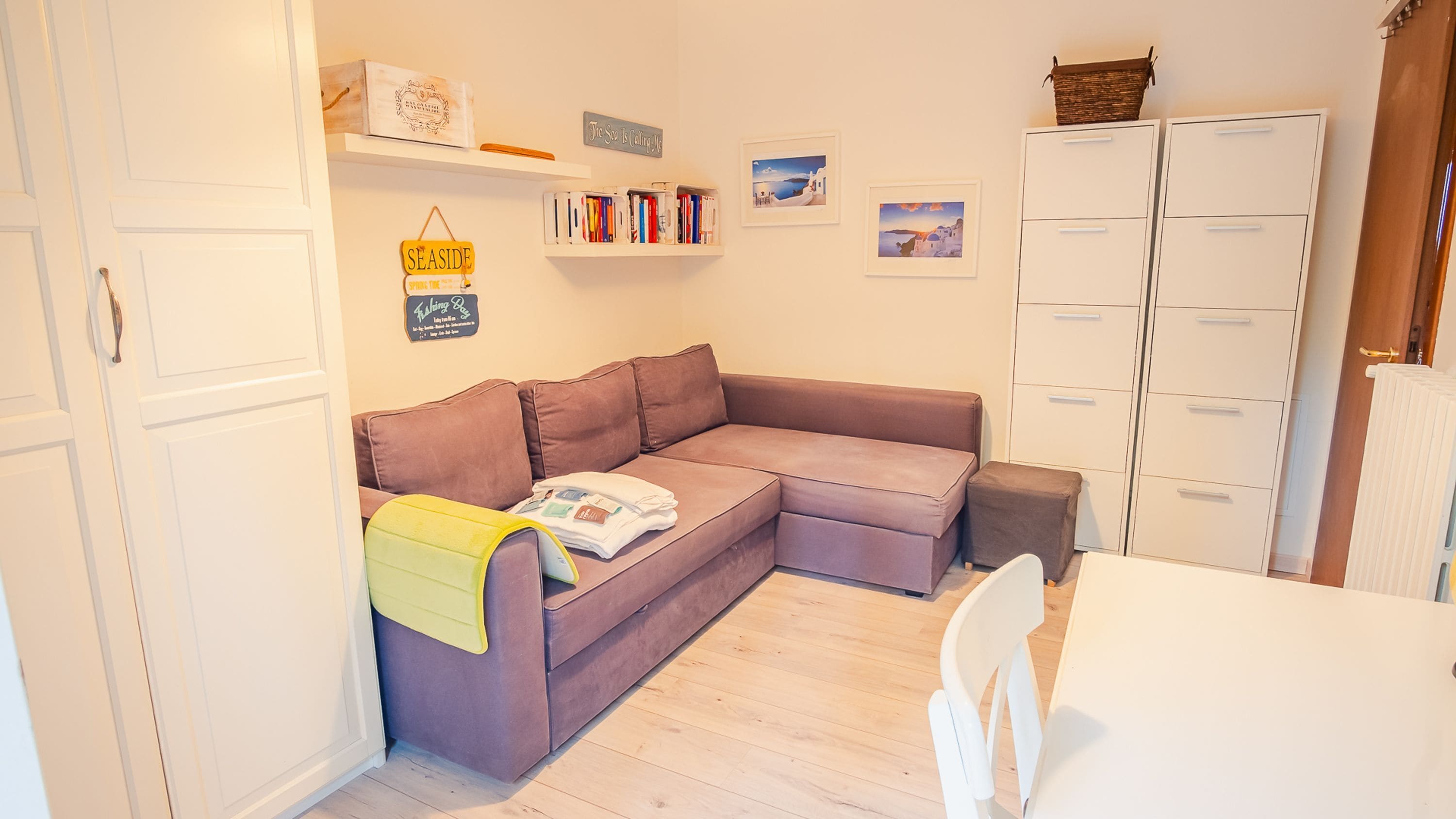 A cozy living room with a brown sofa, a white table, and a bookshelf with books and decorative items.