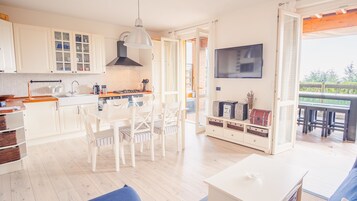 A modern kitchen with white cabinets, a dining area with white chairs, and a TV mounted on the wall.