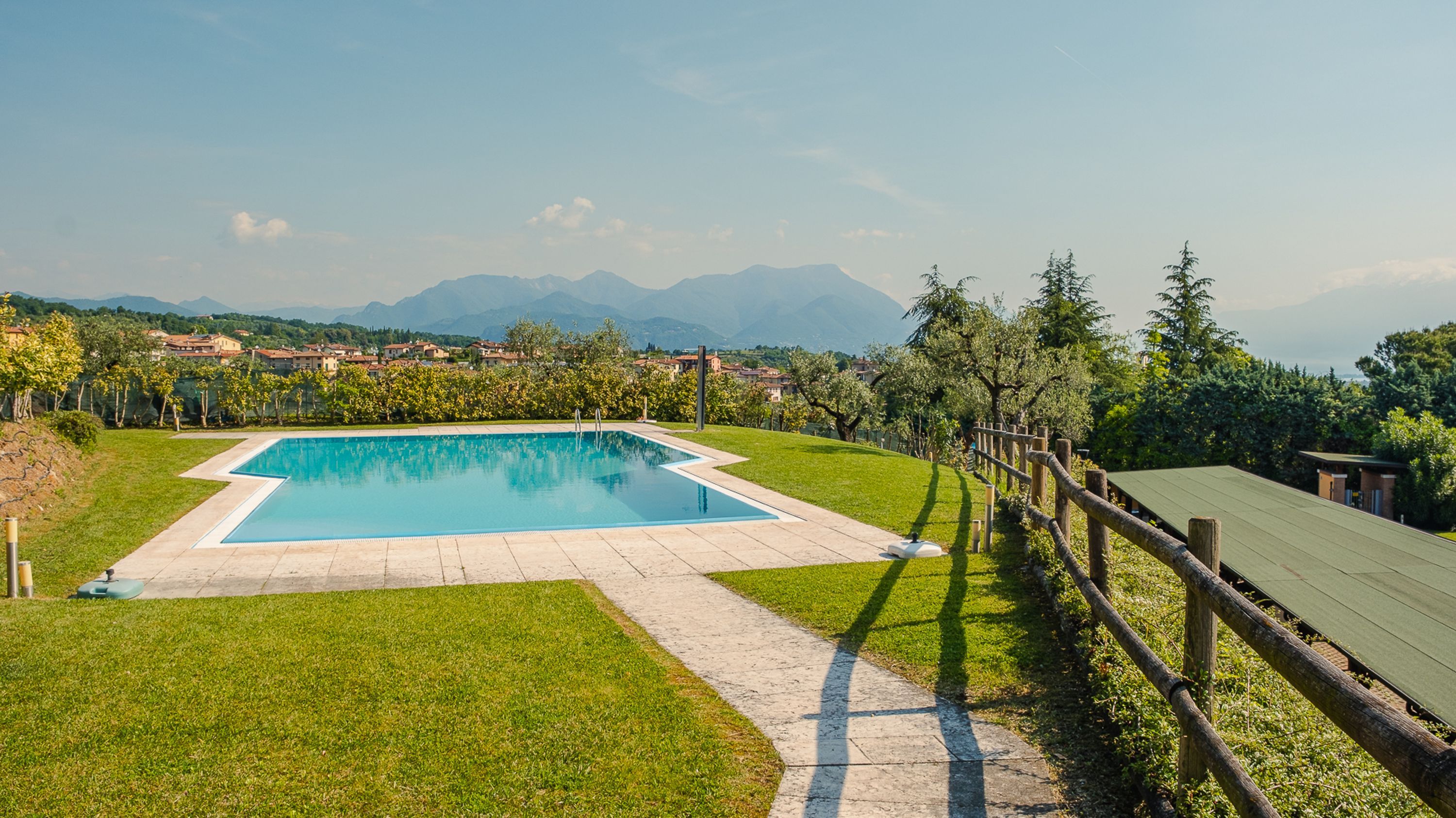 Une piscine rectangulaire entourée d’une zone pavée, d’une terrasse en bois et offrant une vue sur les montagnes lointaines.