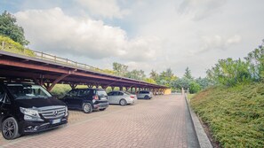 Ein Parkplatz mit Fahrzeugen, einem überdachten Gang und Grünflächen.