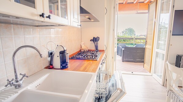 A kitchen with a double sink, a stove, and a dishwasher. There is a window overlooking a patio area.