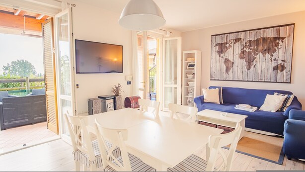 Ein modernes Wohnzimmer mit Esstisch in Weiß, blauem Sofa und einem flachbildfernseher an der Wand.