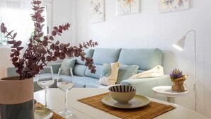 A living room with a light blue sofa, a white coffee table, and a small side table with a lamp. There are three framed floral artworks on the wall. - Bungalow Pink Punta Prima (Punta Prima)