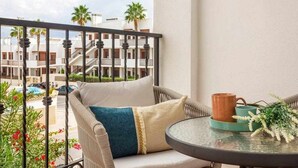 A balcony with a wicker chair, a small table, and a view of a residential area with palm trees and buildings. - Bungalow Pink Punta Prima (Punta Prima)