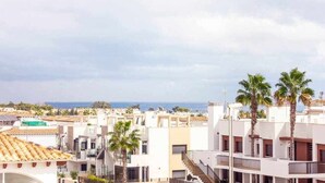 A residential area with white buildings, palm trees, and a view of the sea. - Bungalow Pink Punta Prima (Punta Prima)