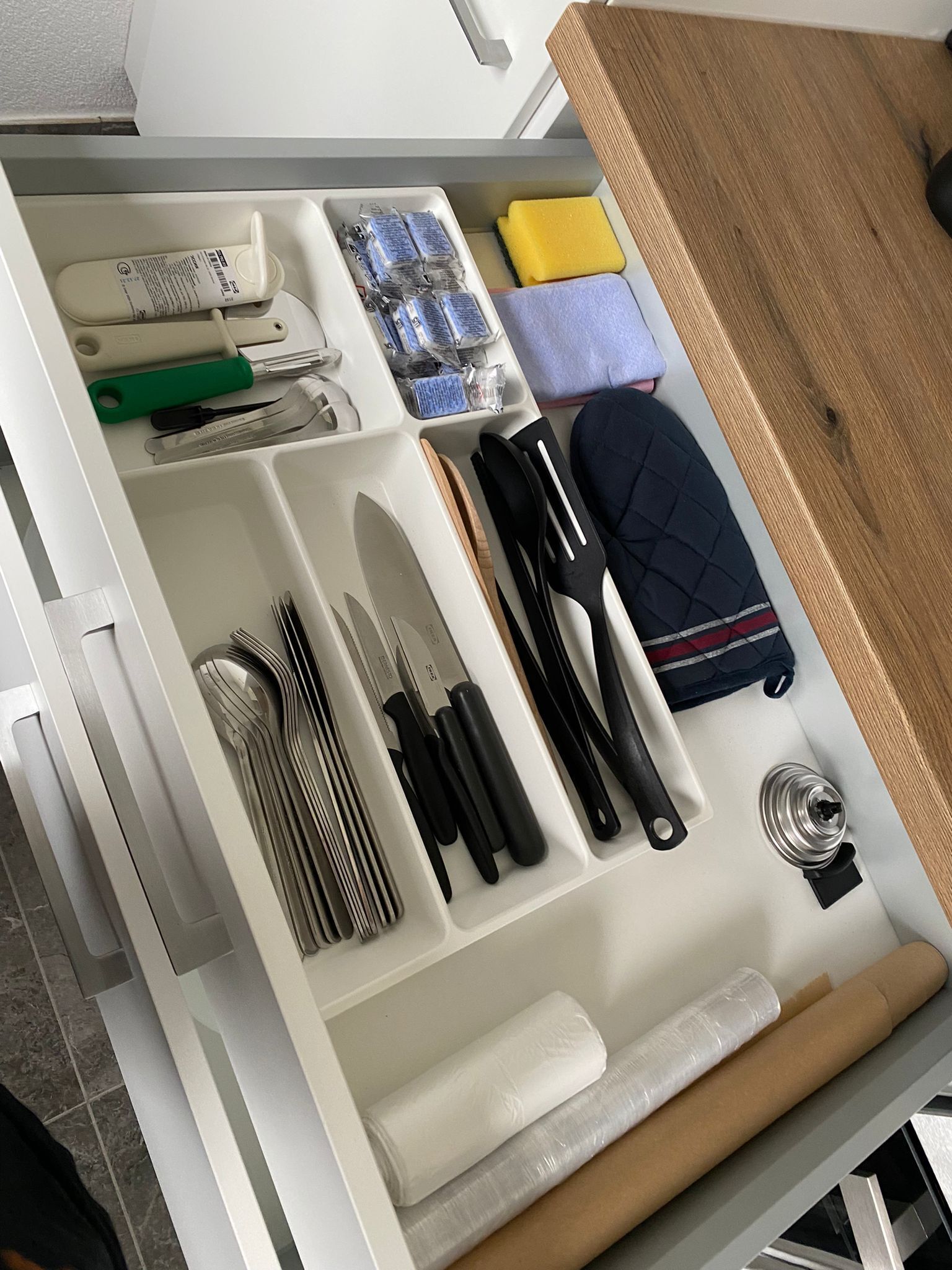 A kitchen drawer with utensils, a rolling pin, a coffee maker, and a blue oven mitt.