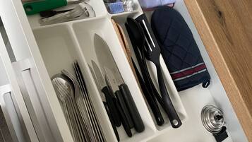 A kitchen drawer with utensils, a rolling pin, a coffee maker, and a blue oven mitt.