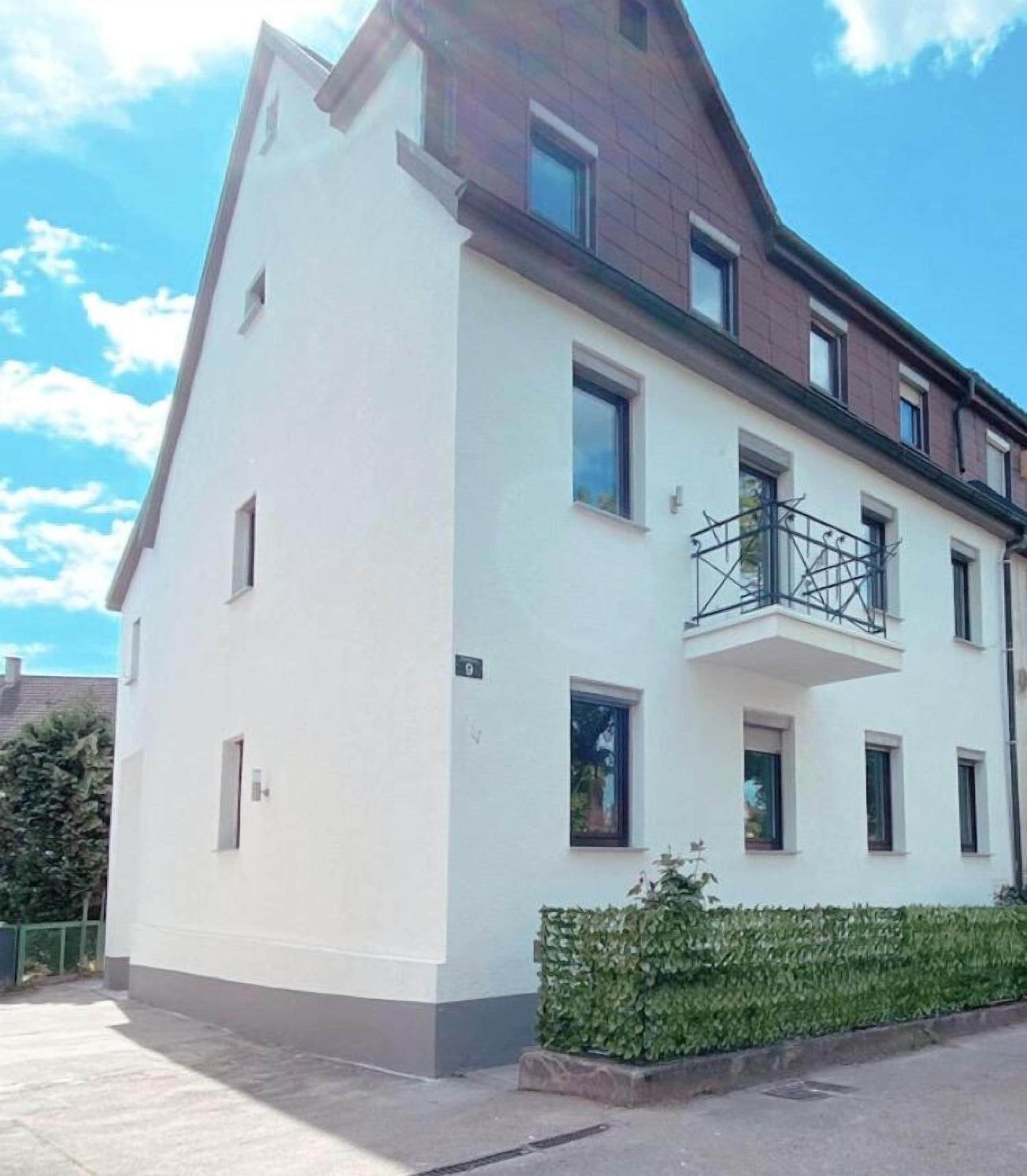 En toetagers bygning med en hvid facade, en balkon på anden sal og et lille haveområde foran.
