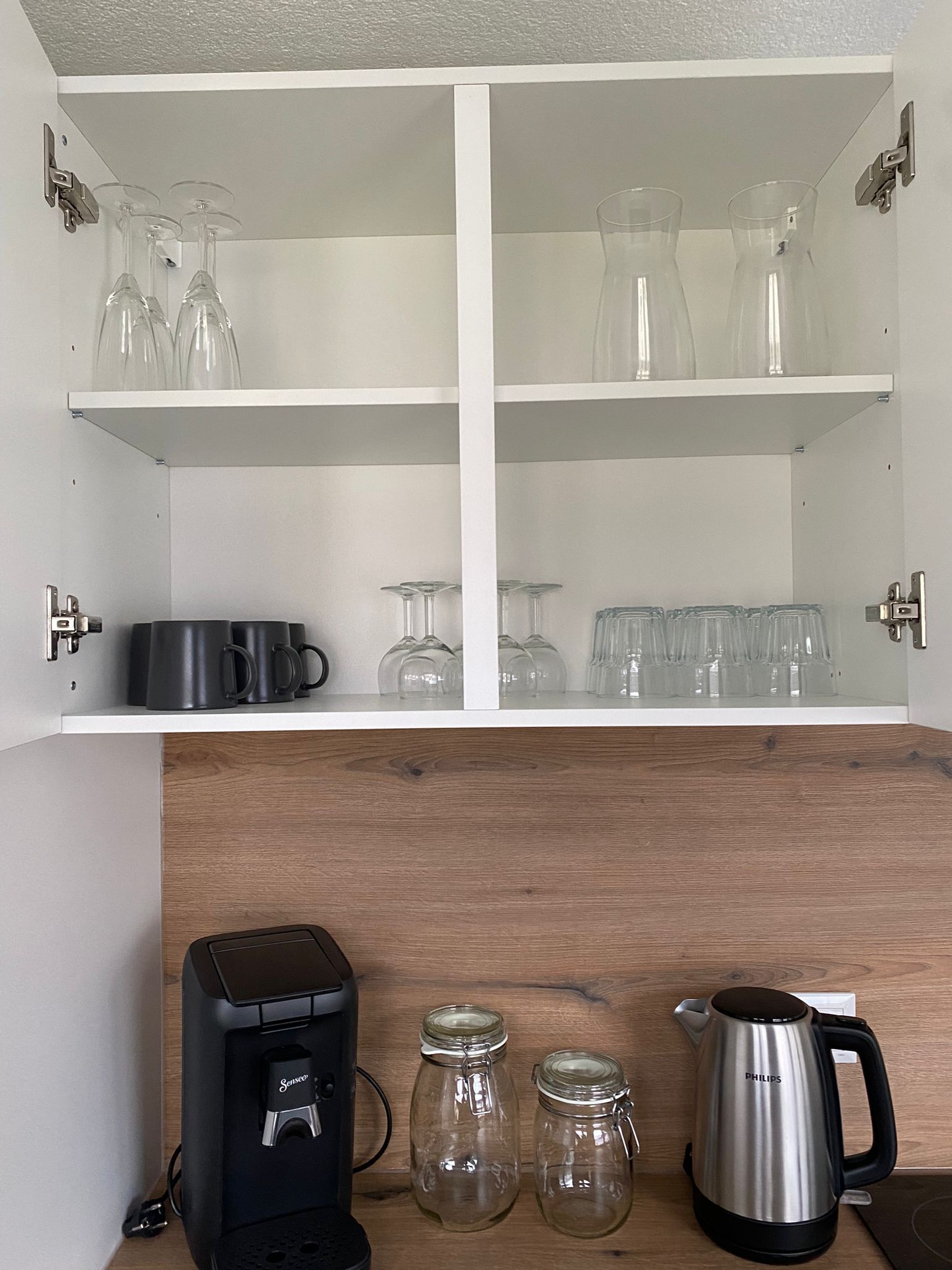 Una cocina con una cafetera, dos tarros de vidrio y un hervidor sobre la encimera.