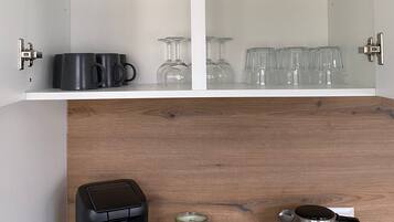 Una cocina con una cafetera, dos tarros de vidrio y un hervidor sobre la encimera.
