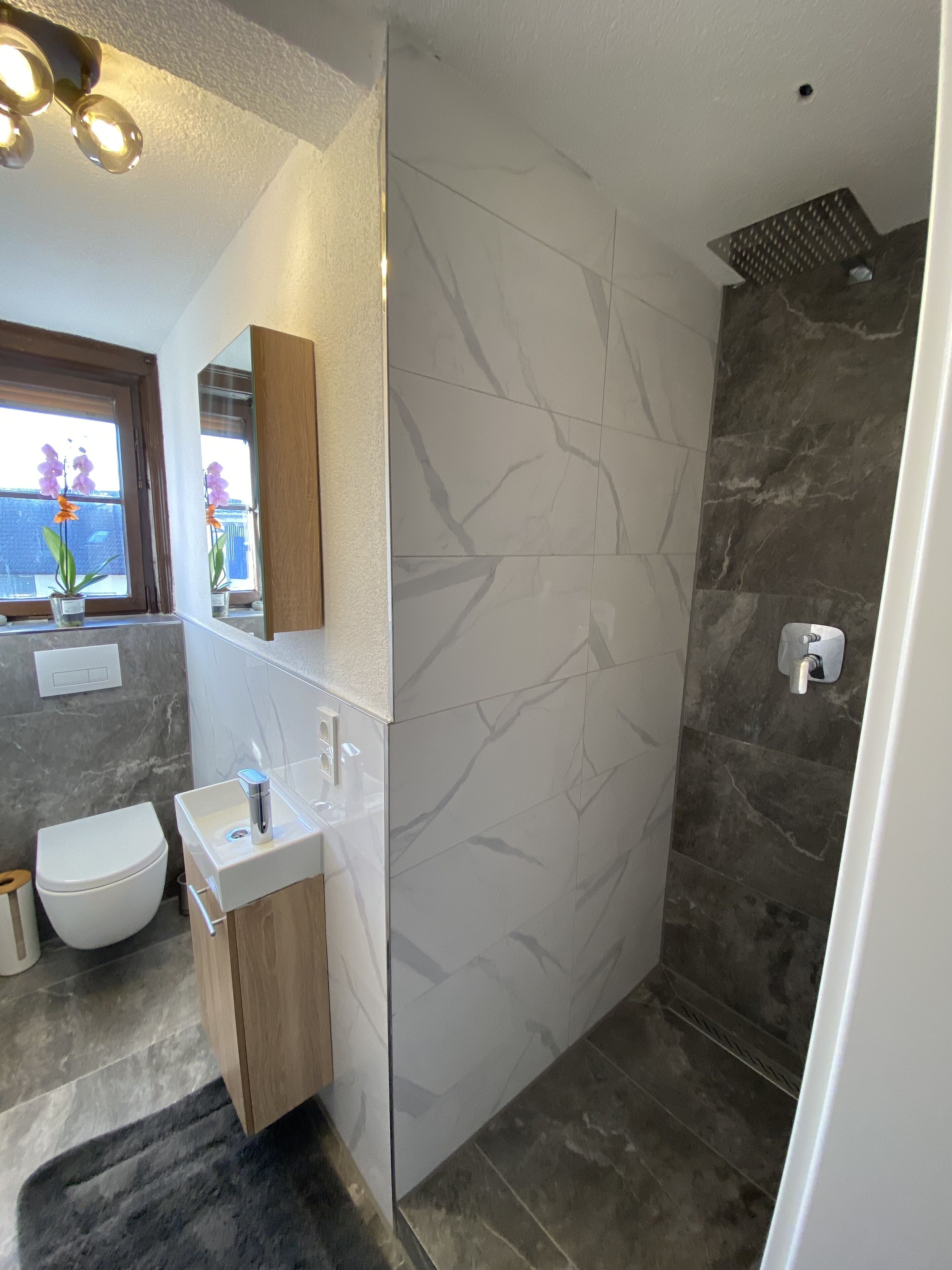 Ein modernes Badezimmer mit Marmorwand, Holzwaschtisch, weißer Toilette und Duschbereich.